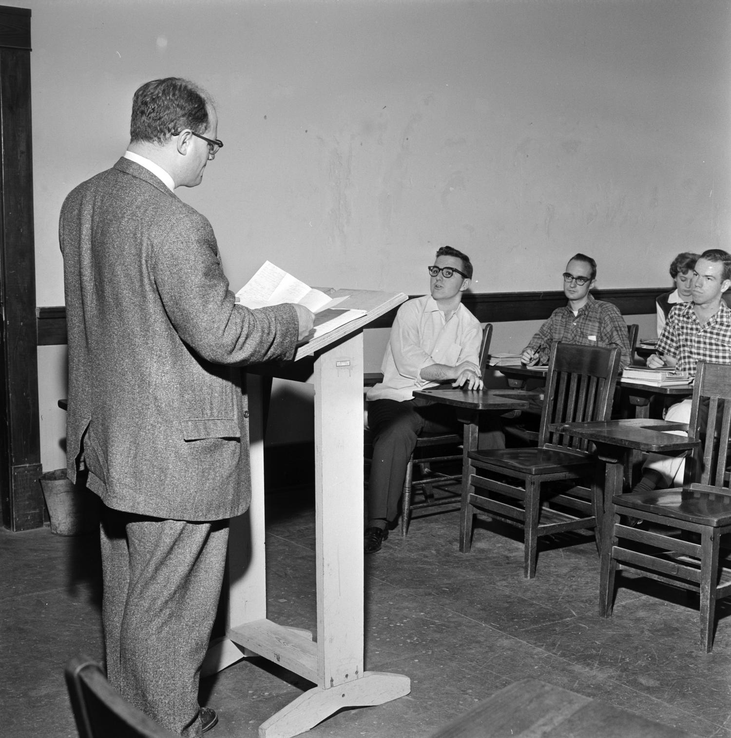 Man at podium lecturing students in chairs in front of him