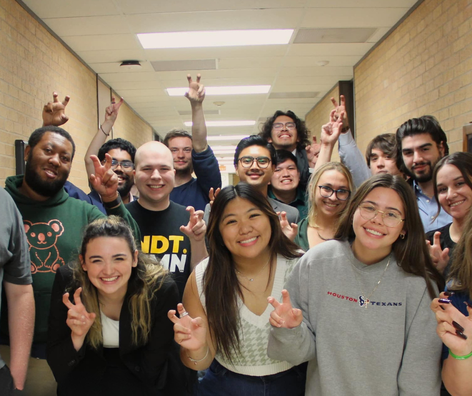 UNT Debaters posing in hallway smiling with UNT claw raised