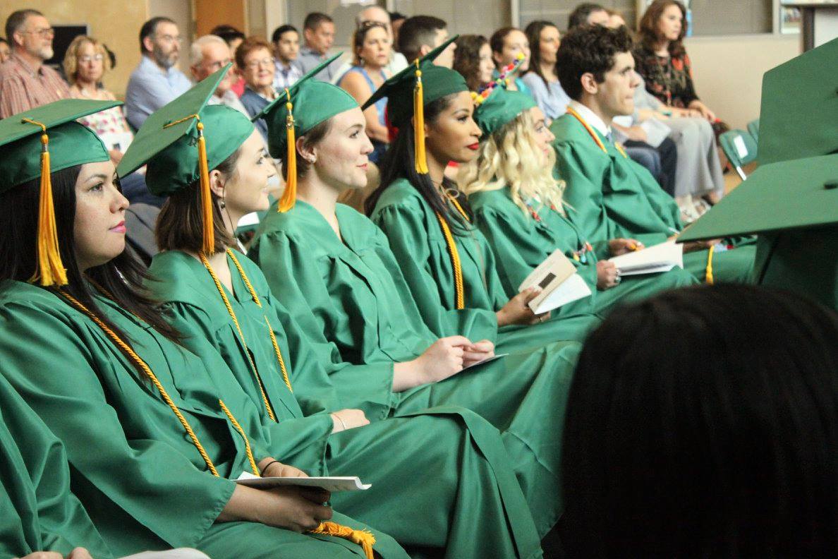 Graduates sitting at ceremony in green caps and gowns