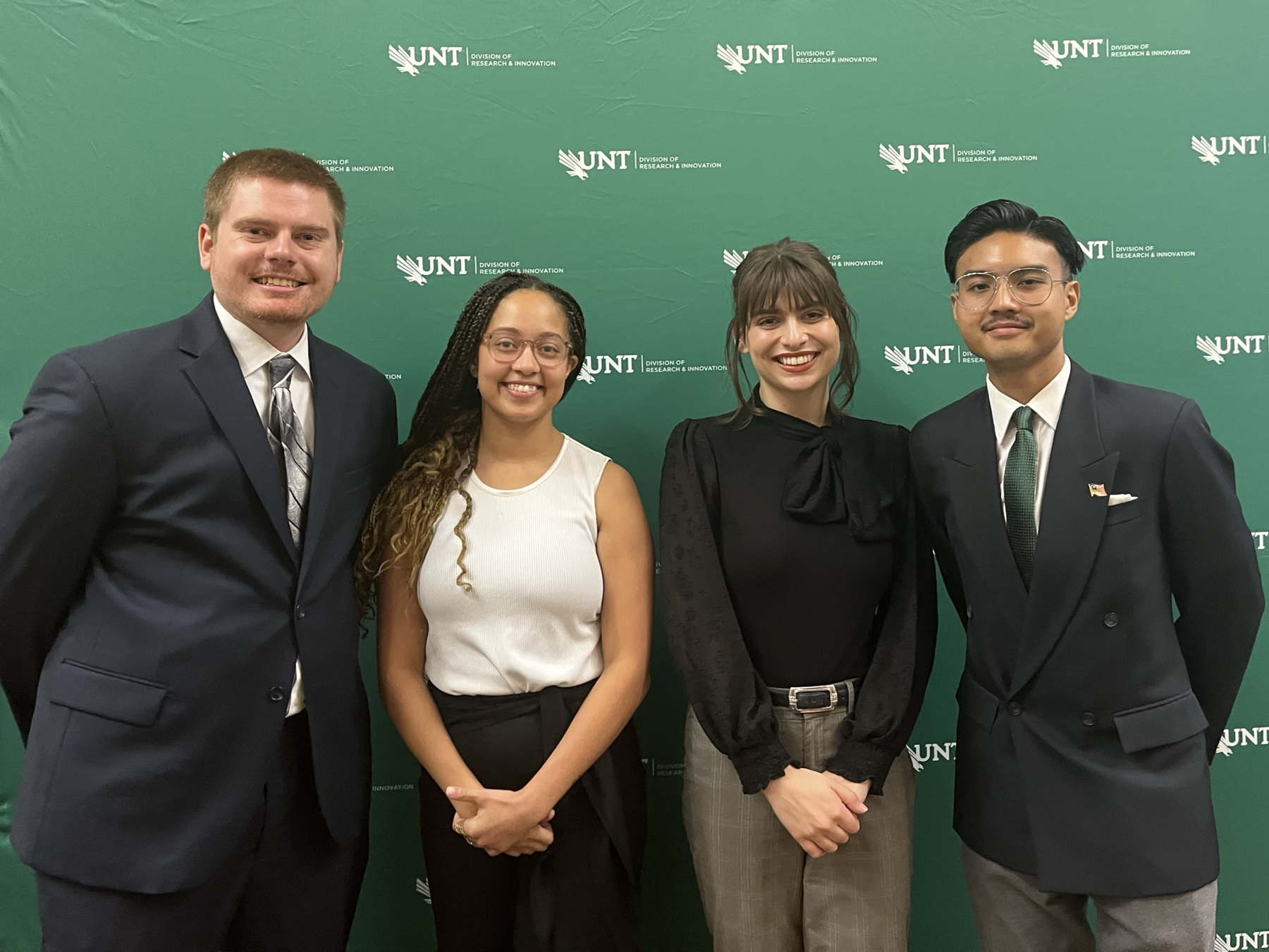 Trevor Holcombe, Bri Branscomb, Meredith Stuart, and Adrian Tam in front of green UNT photo background.