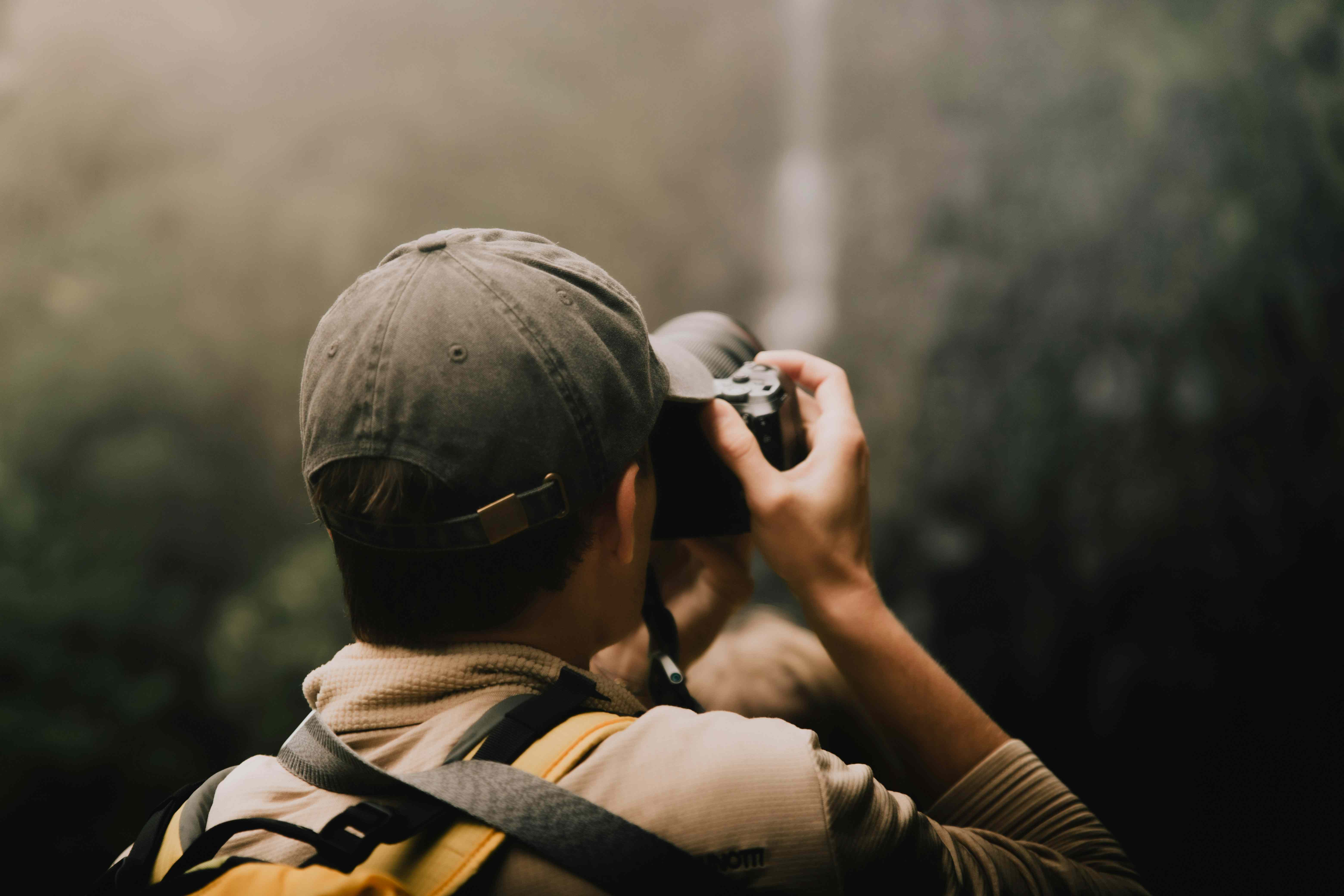 Student with backpack and cap taking a photograph outdoors with a digital camera