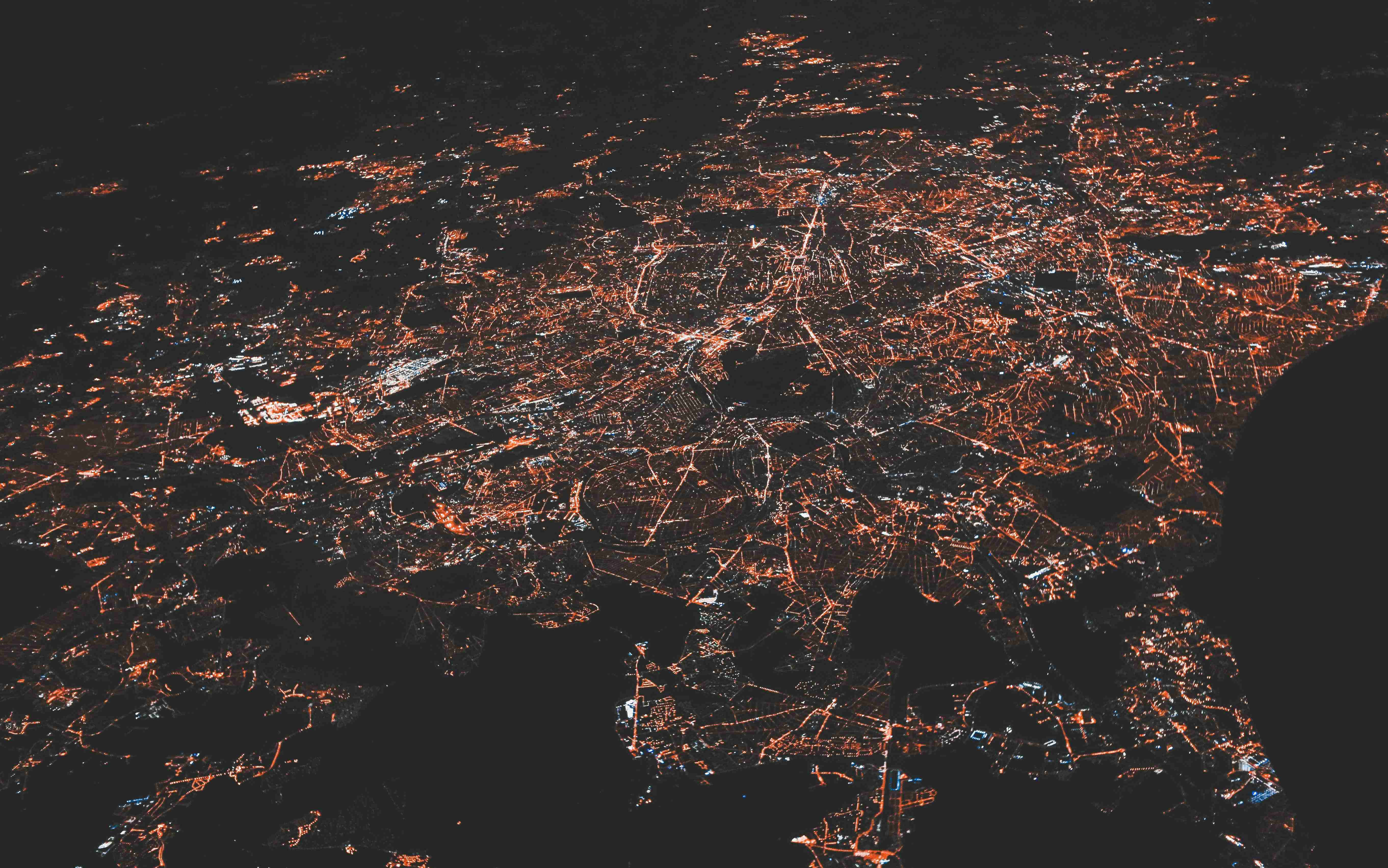 Night aerial view of a brightly lit city network with glowing orange and white streets