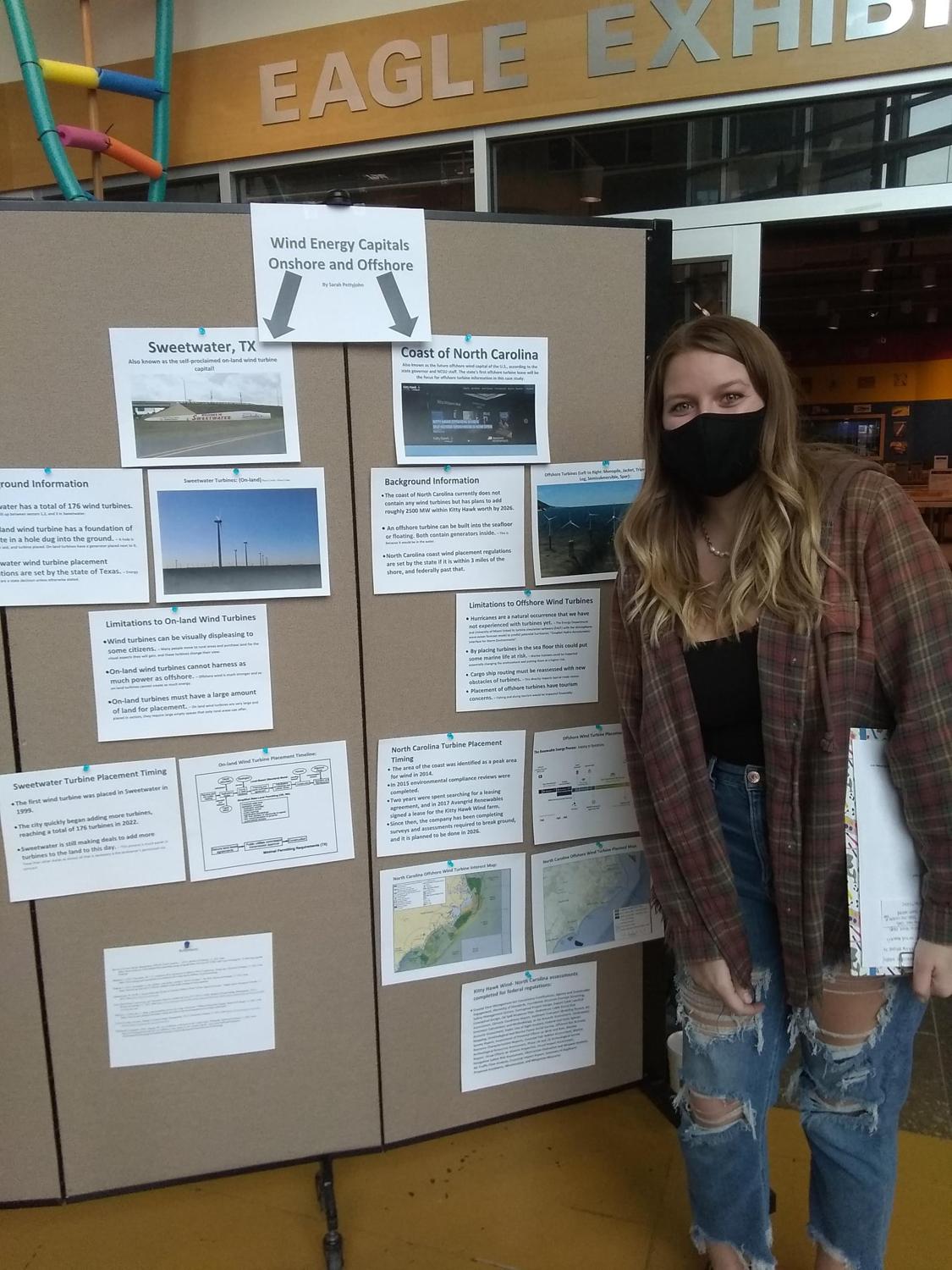 A masked student poses in front of a poster presentation