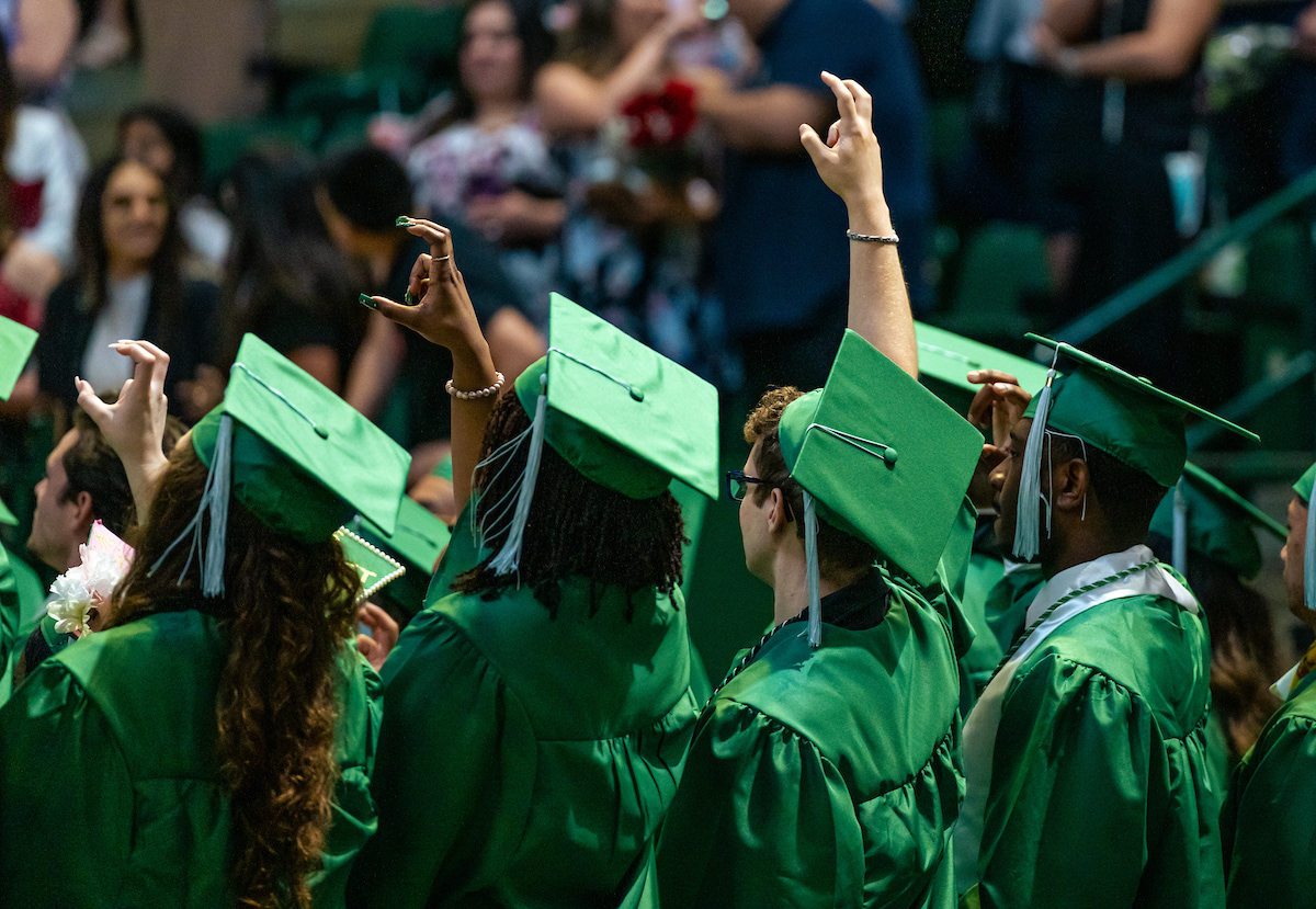 Students in green caps raising hands