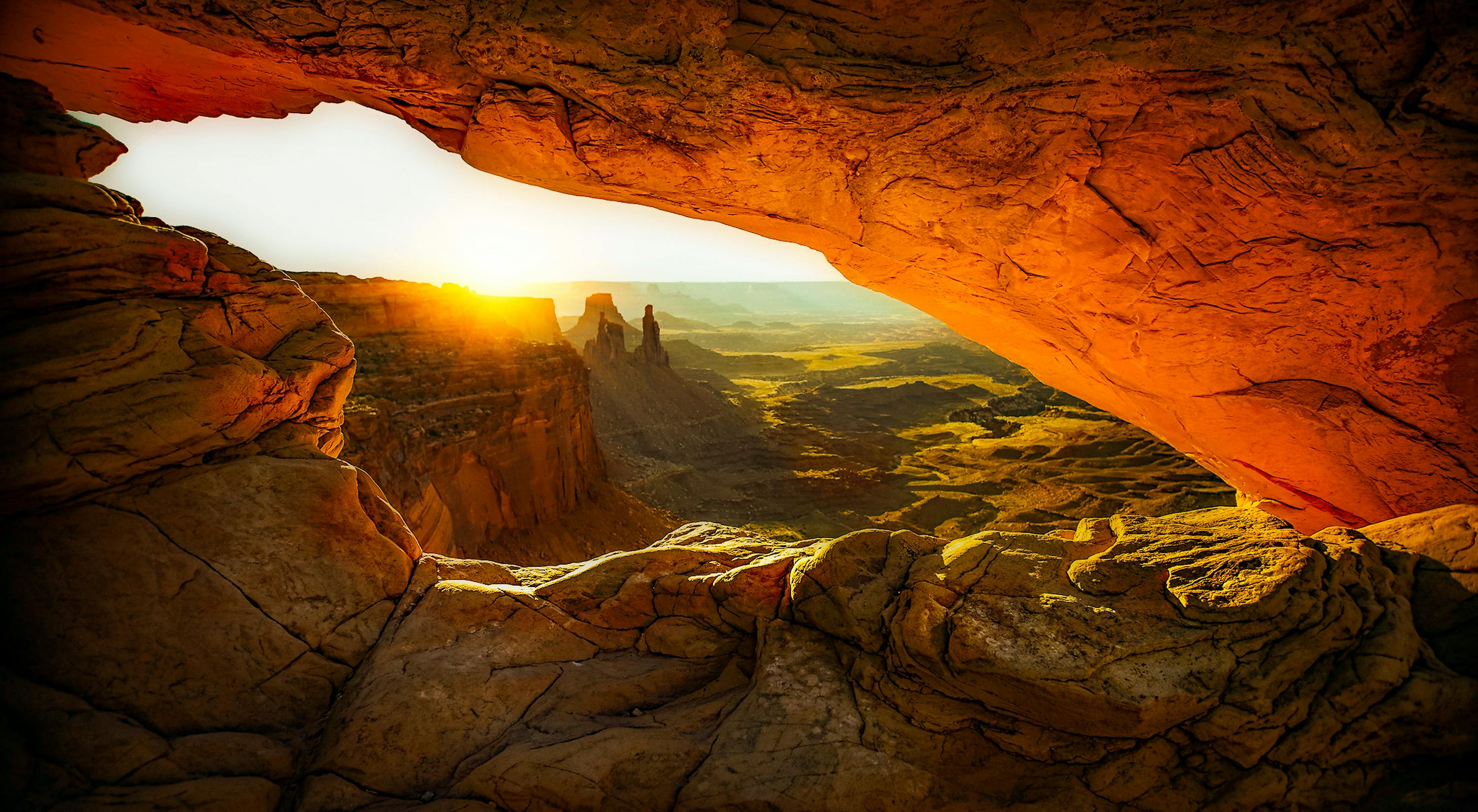 Sunrise view through a rock arch overlooking dramatic canyon landscape