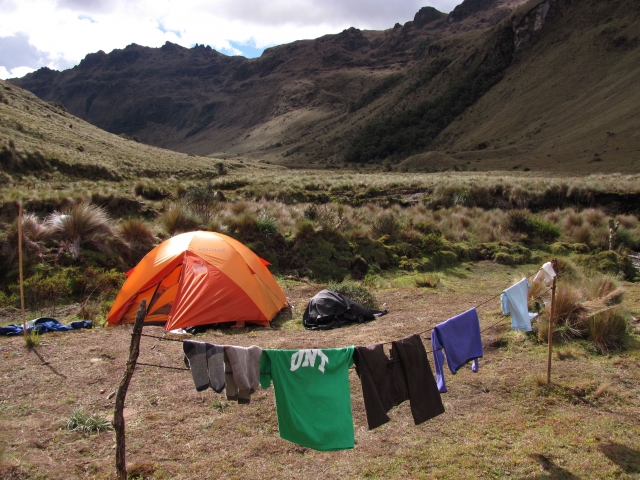Orange tent and clothesline with laundry in a grassy mountain valley campsite