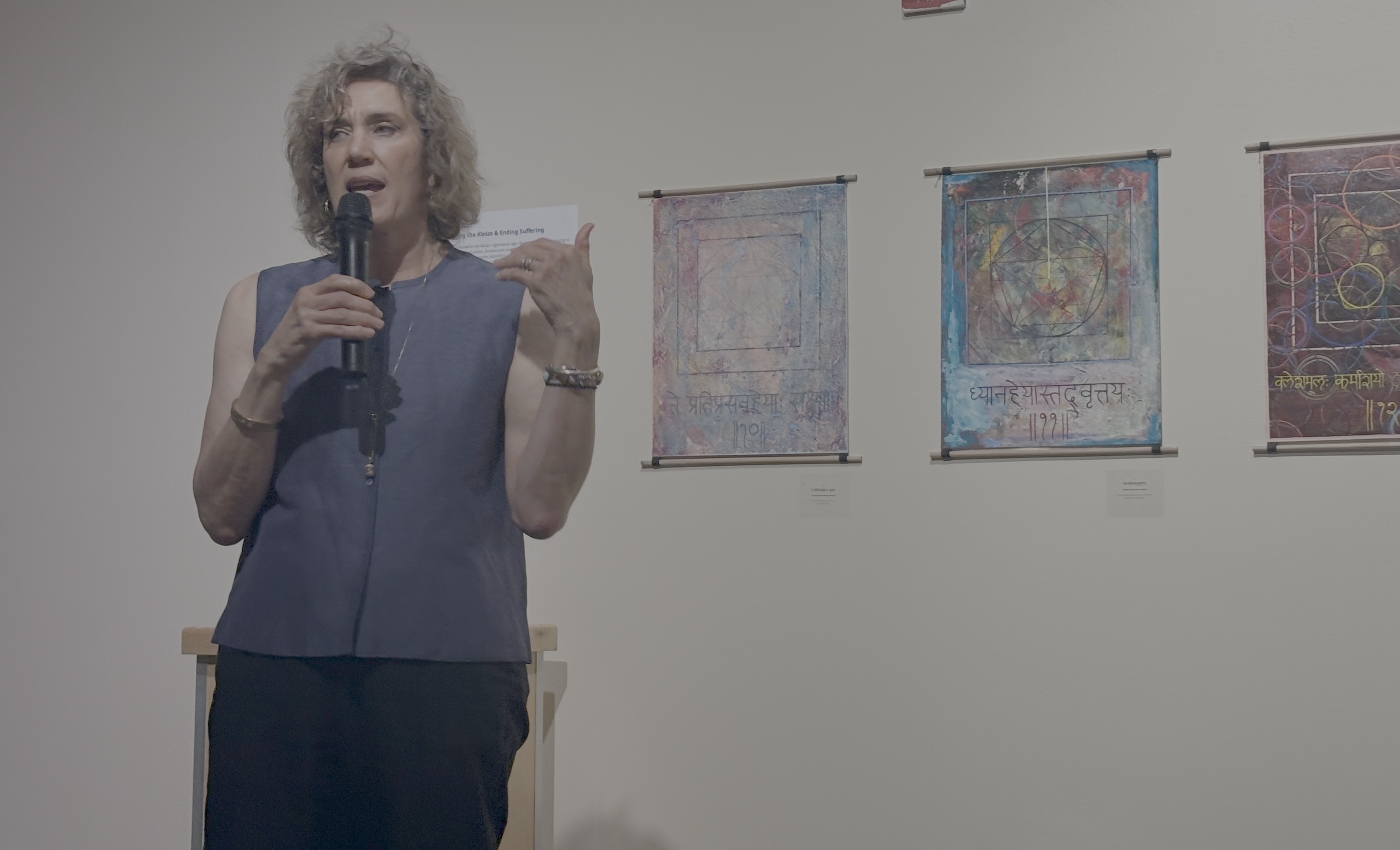 A woman stands in front of three paintings.