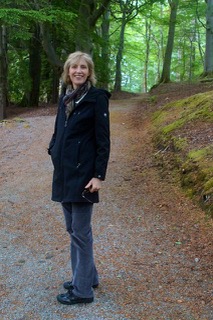 A woman in a blue coat, standing in a forest.